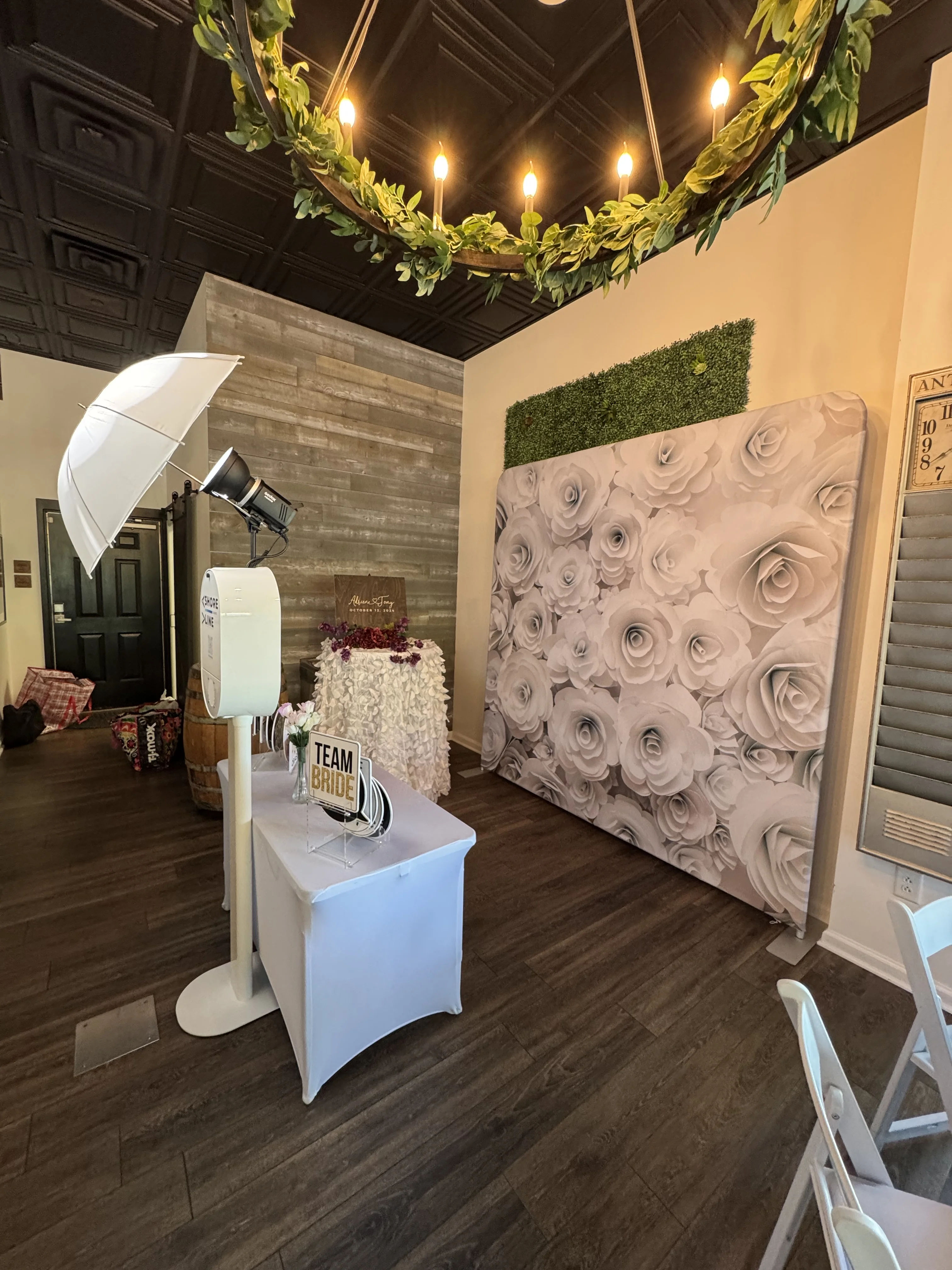 Photo booth setup with white rose floral backdrop at Virginia Beach wedding — Team Bride props and greenery wall